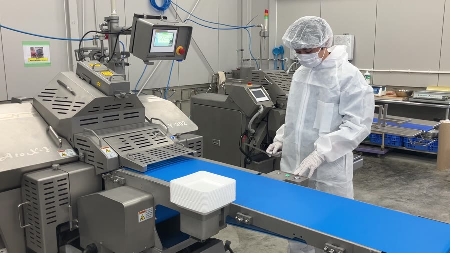 An operator in full hygiene gear running an NCI slicing line in a Japanese food-processing plant, with slices moving down a blue conveyor