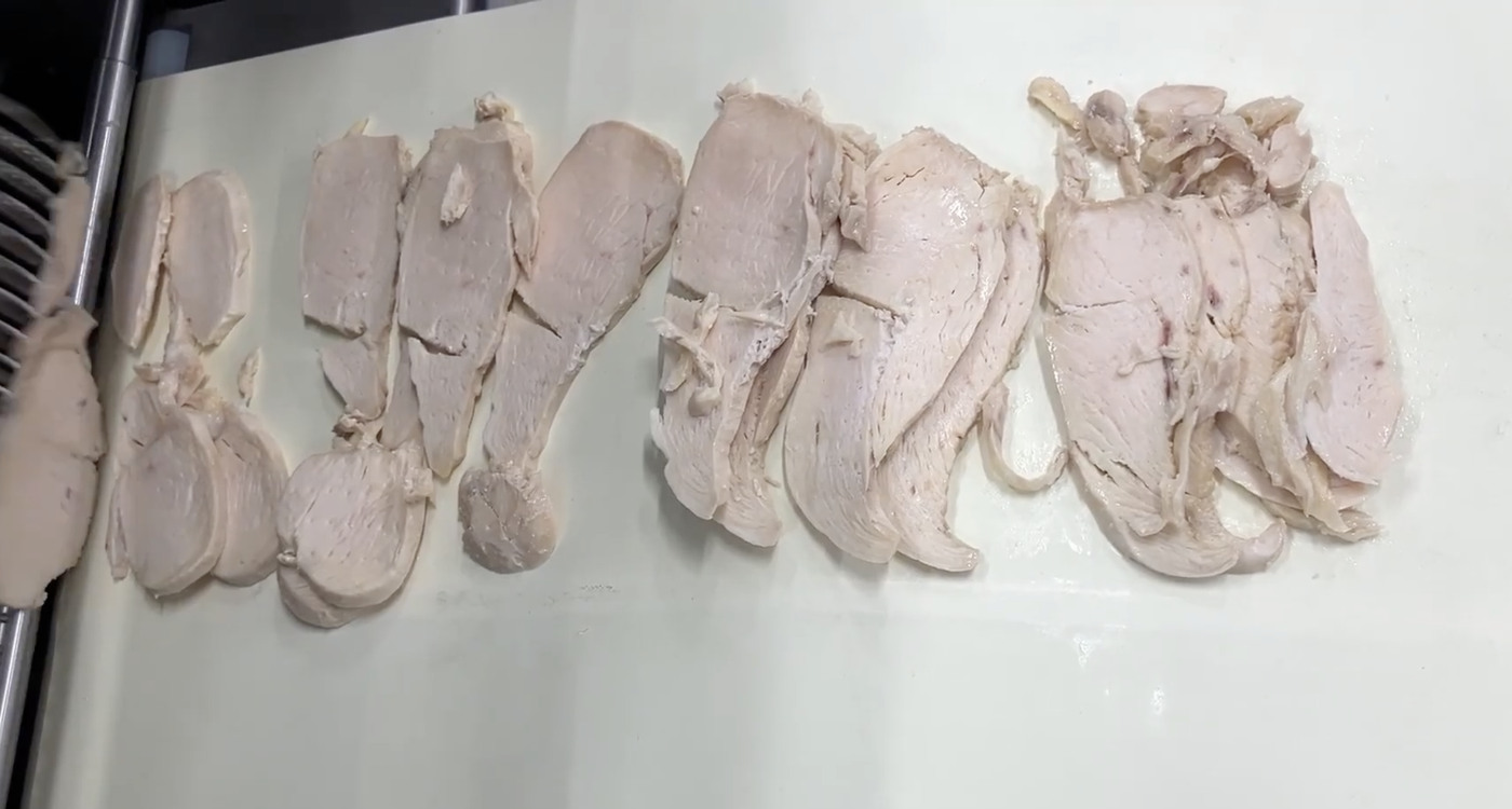 Cooked chicken breast sliced cleanly at 3 mm and laid out in even rows on a white board